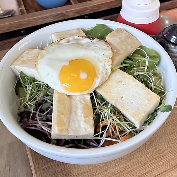 Korean bibimbap bowl with tofu, a fried egg, and various fresh greens and sprouts.