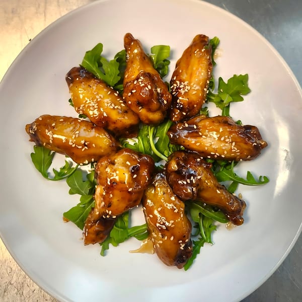 Eight Korean chicken wings, glazed and topped with sesame seeds, arranged on a bed of arugula.