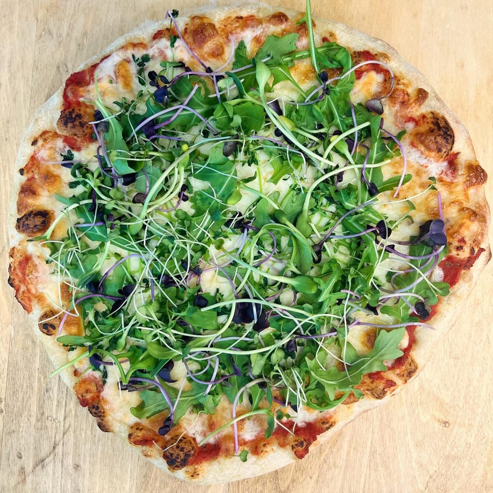 A Korean-style pizza from The Soop, topped with fresh arugula and microgreens on a wooden surface.