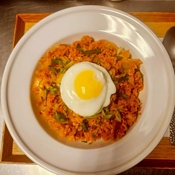 Kimchi fried rice with green onions and a sunny-side-up egg on a white plate at The Soop.