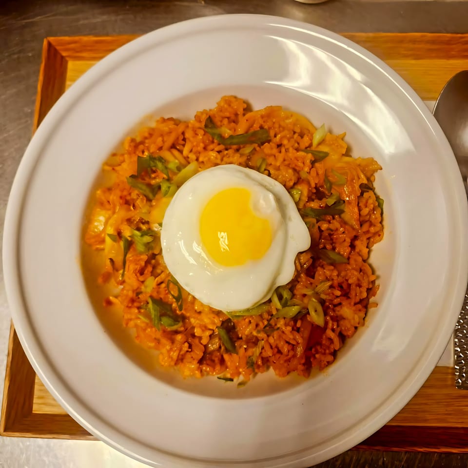 Kimchi fried rice with green onions and a sunny-side-up egg on a white plate at The Soop.