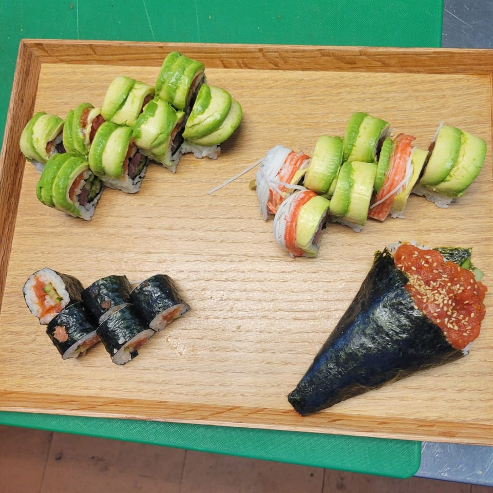 A wooden tray holds various Korean sushi rolls, including avocado-topped, salmon, and a spicy tuna hand roll.