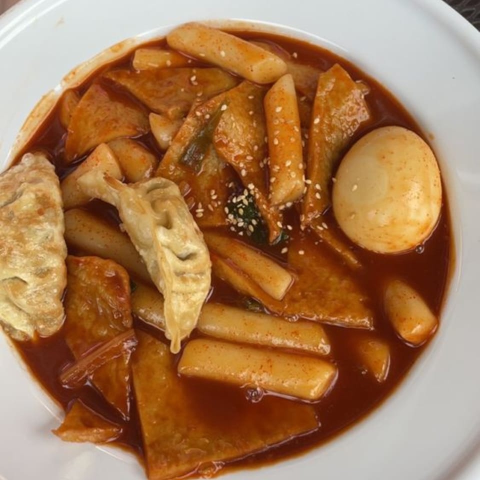 A close-up of The Soop's Tteokbokki with rice cakes, fish cakes, dumplings, and a boiled egg in red sauce.
